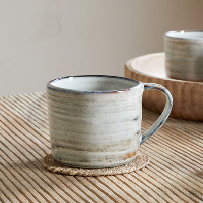 Ceramic mug on a woven mat with a wooden surface and blurred background