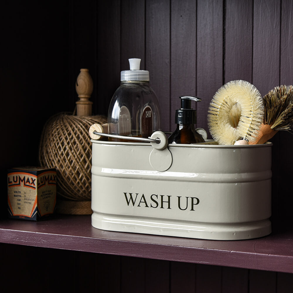 Beige metal wash-up basket with cleaning supplies on a wooden shelf.