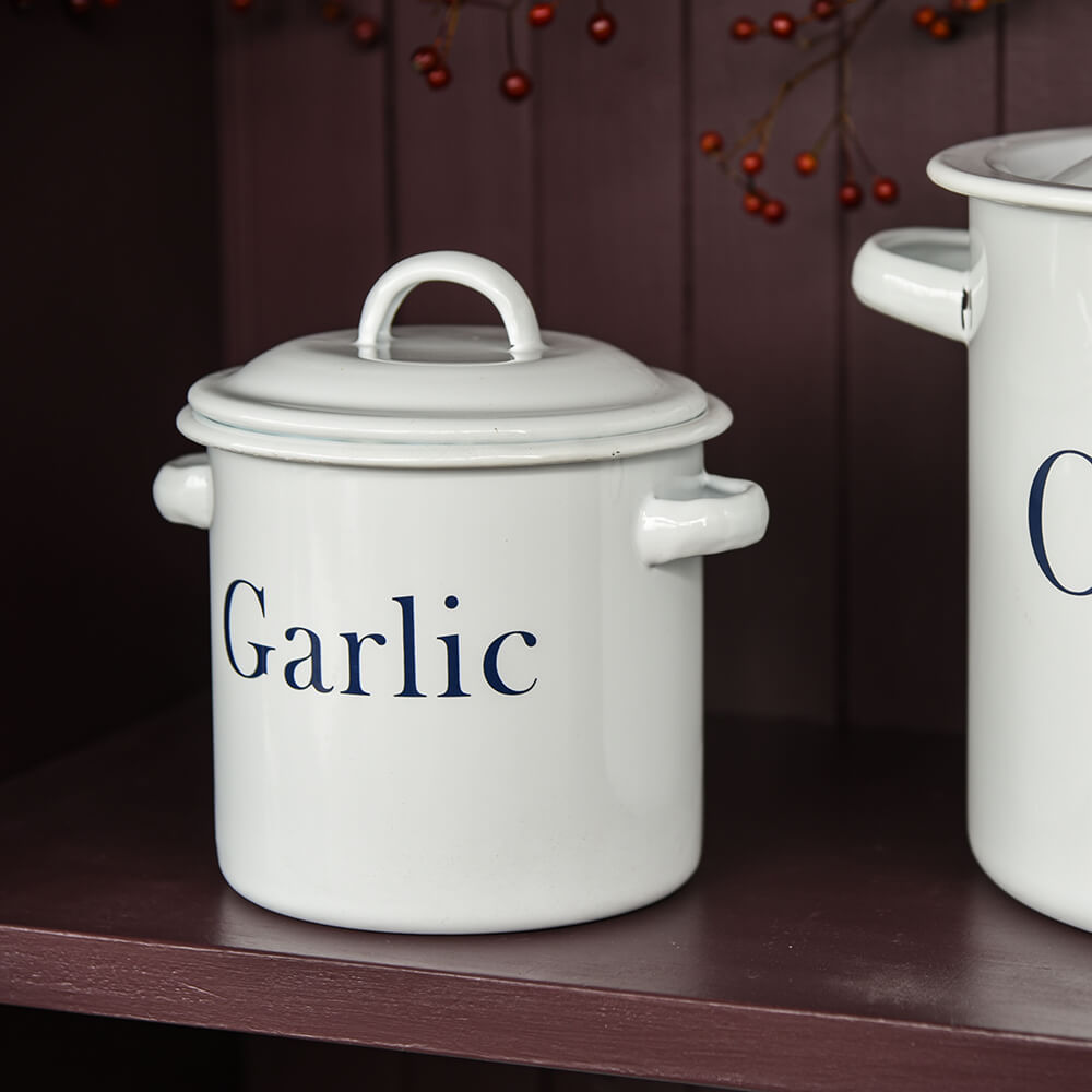 White ceramic container labeled 'Garlic' on a wooden shelf with a dark background.