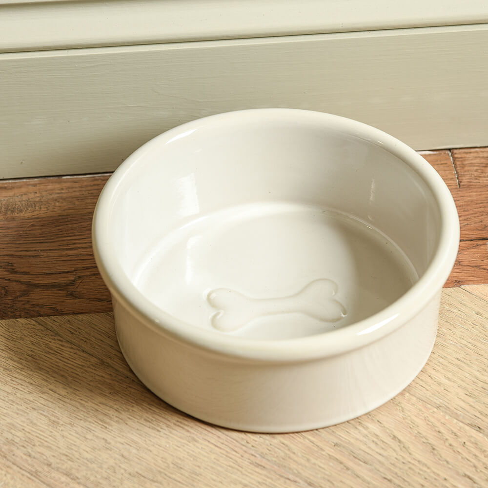 White ceramic pet bowl with a dog bone design on a wooden floor.