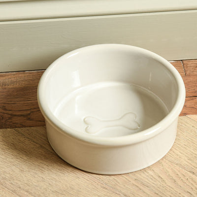 White ceramic pet bowl with a dog bone design on a wooden floor.