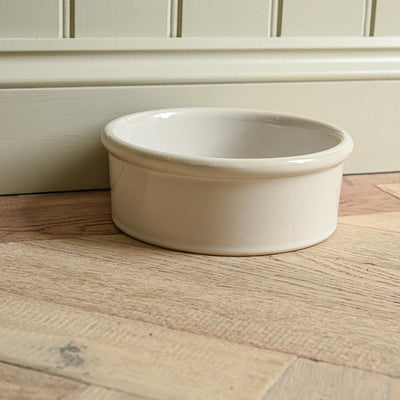 White ceramic bowl on a wooden floor against a beige wall.