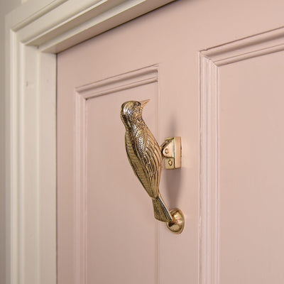 Woodpecker door knocker made from solid brass on a pink front door