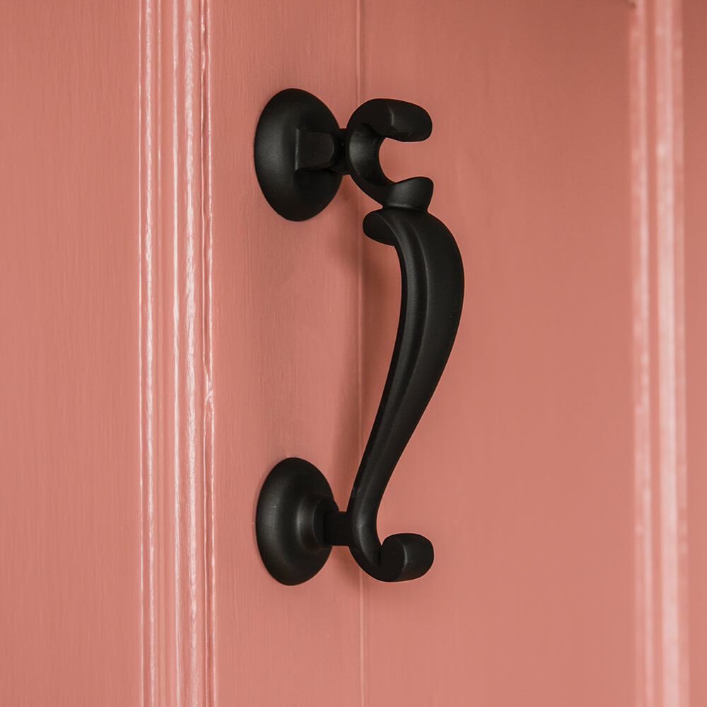 Black door knocker in the classic dctors style shown on a salmon pink door