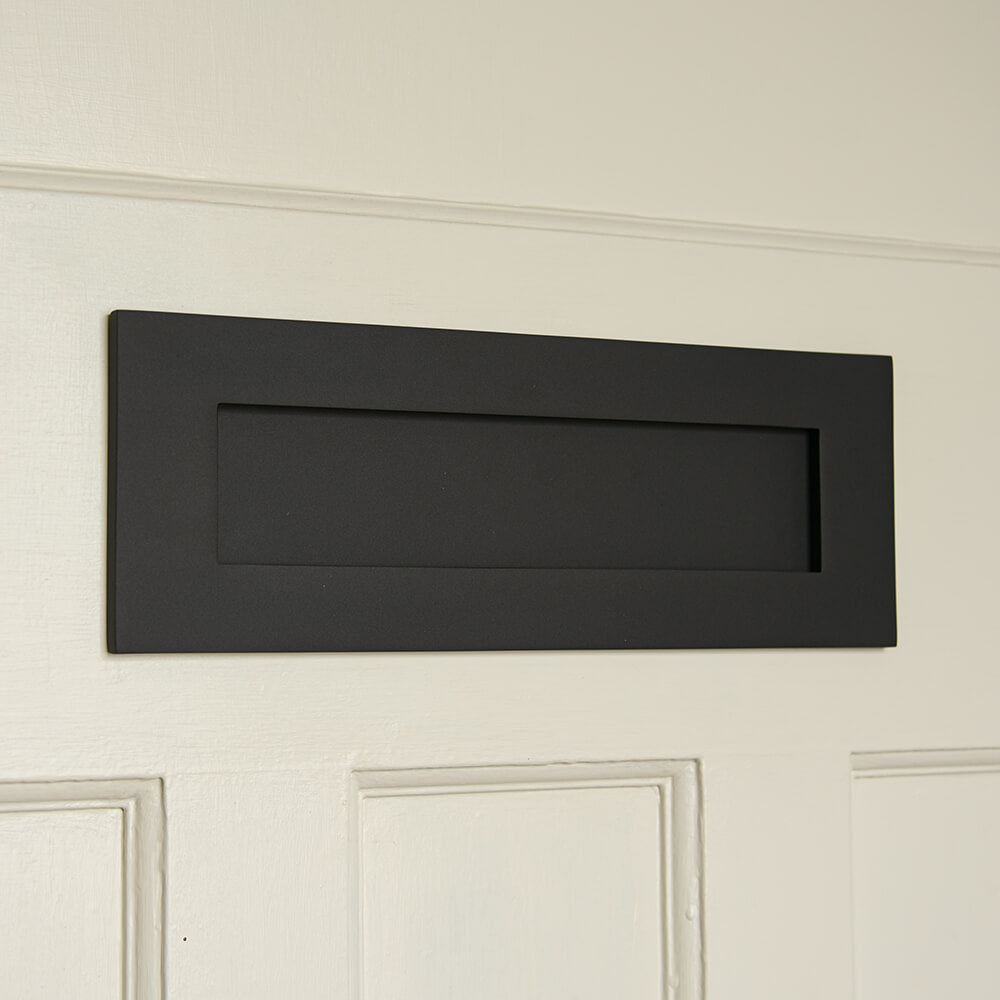 A matt black rectangular letterplate on a cream panelled door