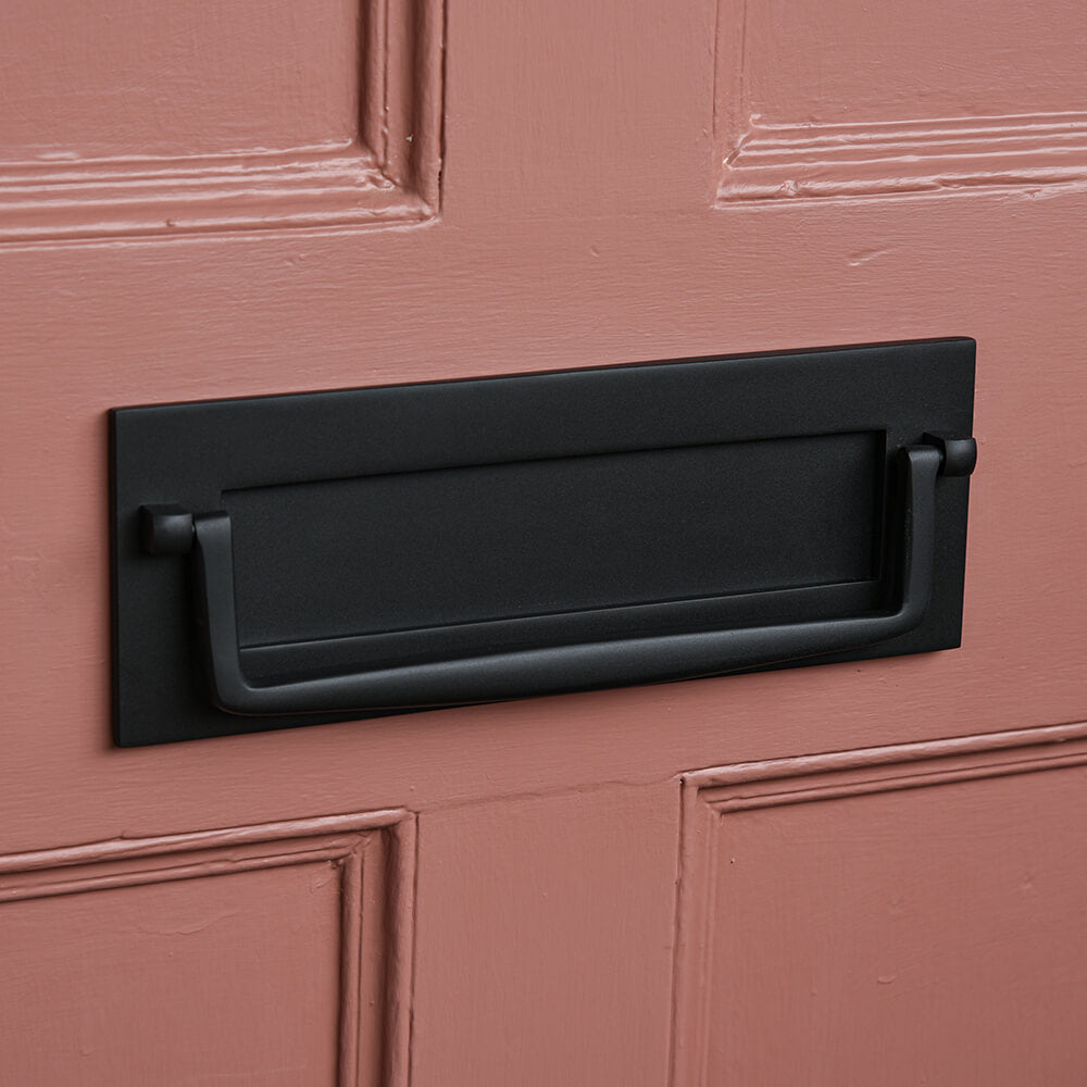 Black letterbox with drop handle on a pink door