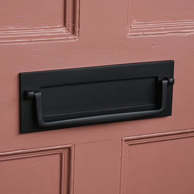 Black letterbox with drop handle on a pink door