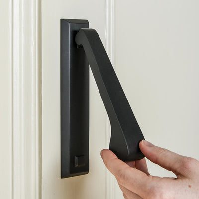 Hand using a black door knocker on a beige door