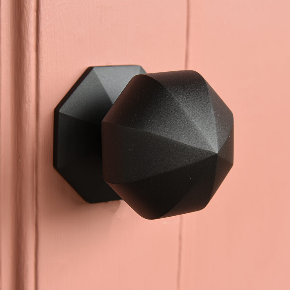 Black geometric door handle on a pink door