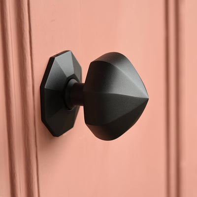 Black geometric door handle on a pink door