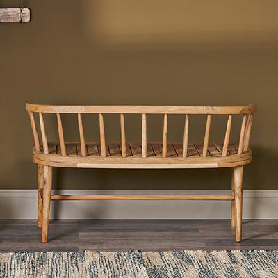 Back view of acacia wood bench with curved backrest sitting on dark wooden floor against olive green wall