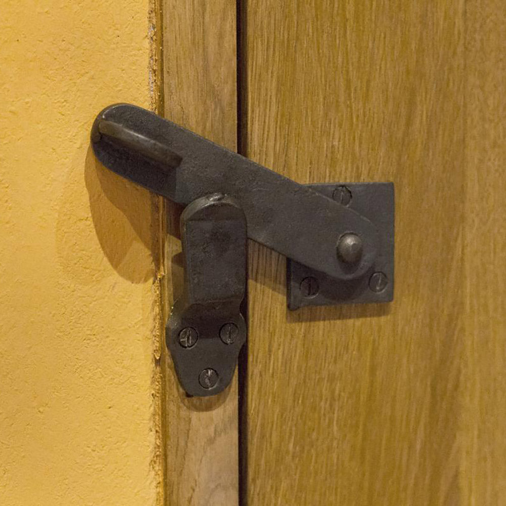 Close up of black beeswax latch on wooden door next to yellow wall