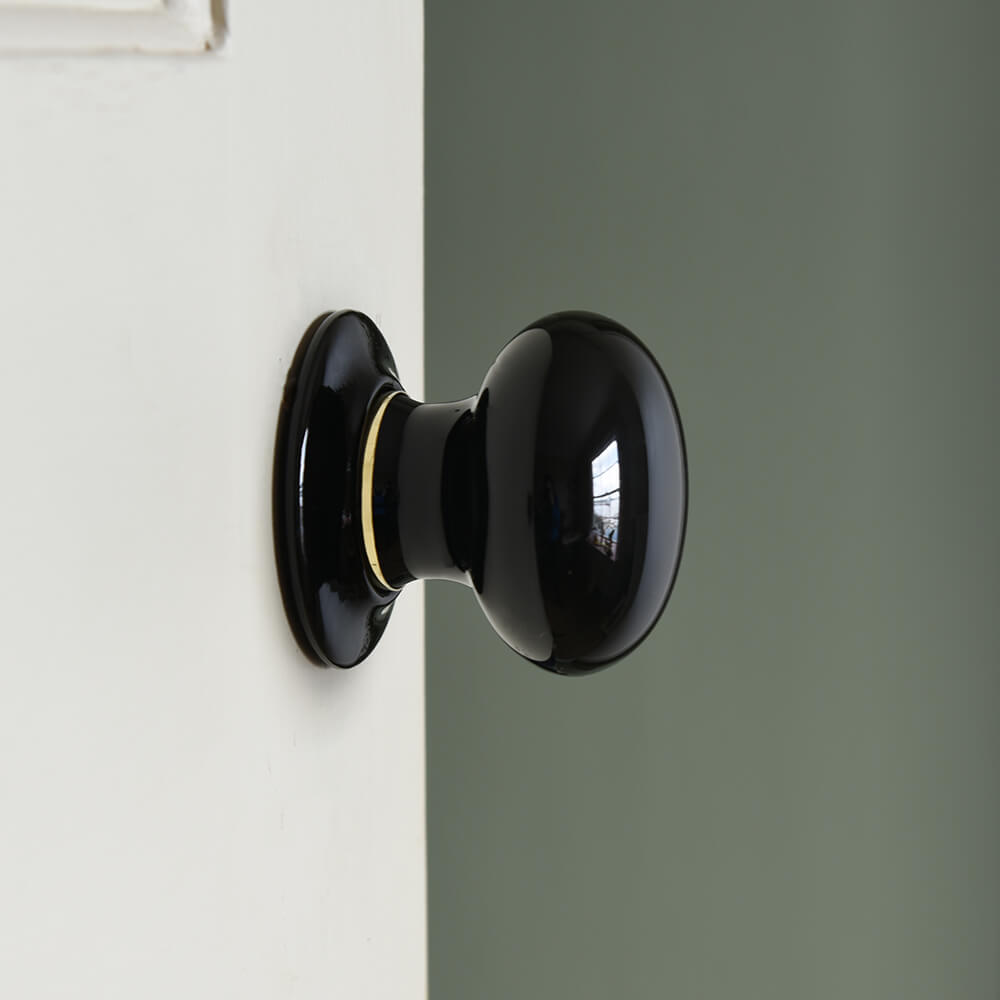 Black cermaic door knobc with a brass rim on a cream door
