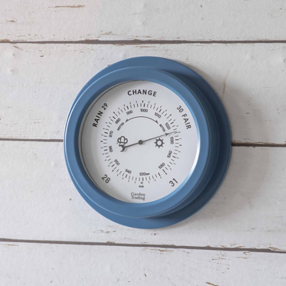 Weather barometer made from powder coated steel and finished in a mid blue hanging against a white panelled wall.