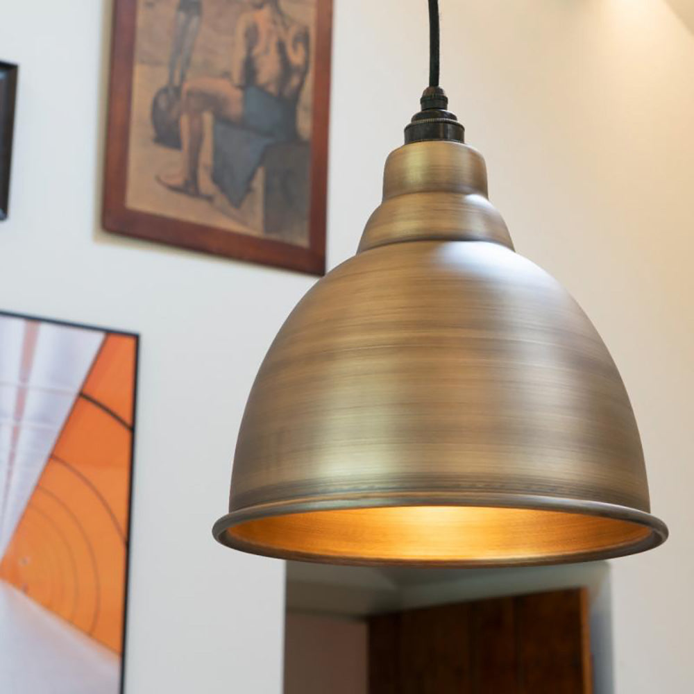 Brushed antique brass Brindley pendant light , illuminated and hanging in situ with a doorway and paintings behind