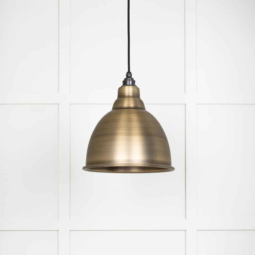 Brushed aged brass Brindley pendant light  hanging from a black fabric cord against a white panelled wall