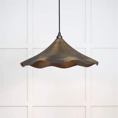 Brushed aged brass flora pendant light hanging from a black fabric cord against a white panelled wall