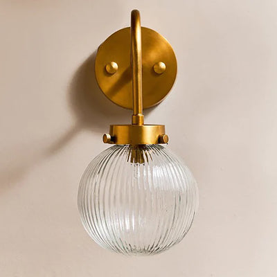 Front view of clear glass globe light with swan neck design and brass fittings against pale background