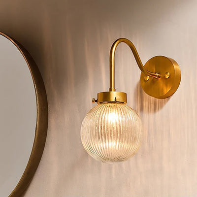 Clear glass globe light switched on with brass fittings and swan neck design against taupe wall next to circular mirror