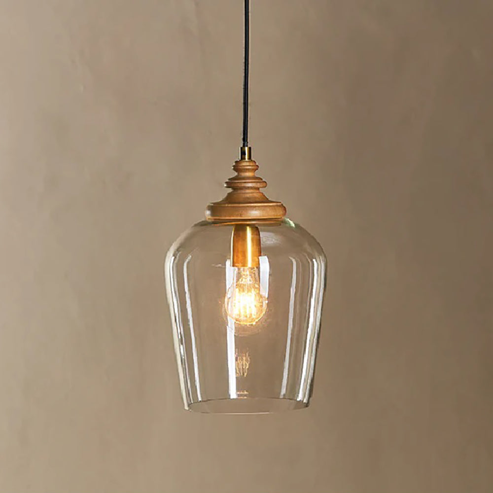 Clear glass pendant light with mango wood and antique brass fittings against a taupe background