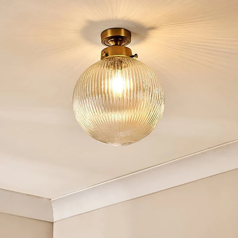 Clear glass globe light switched on with warm glow against brass fittings and pale coloured walls