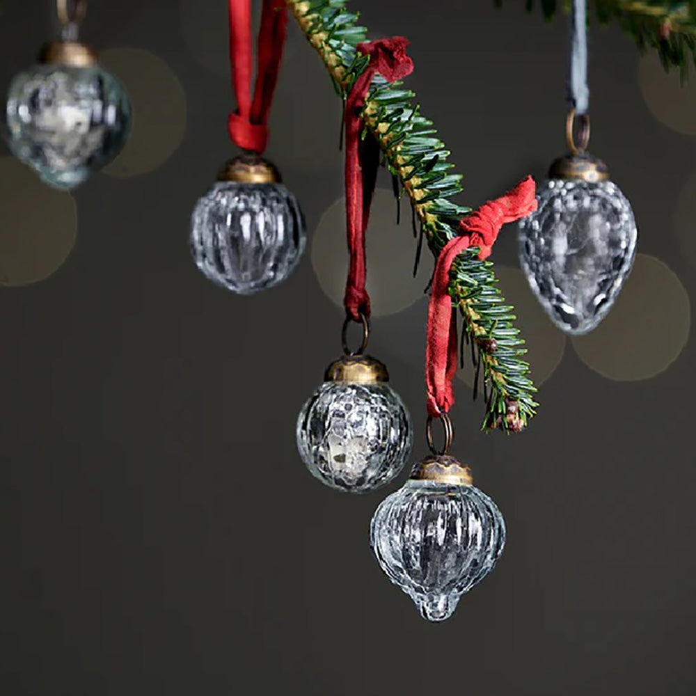 Close up of 12 recycled glass baubles in a mix of round and teardrop designs with clear glass and silver crackle finishes. They hang from a christmas tree branch with coloured ribbons  against a dark blue background
