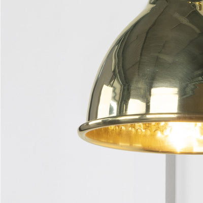 Close up of polished brass wall light, lit up to reflect the hammered internal shade