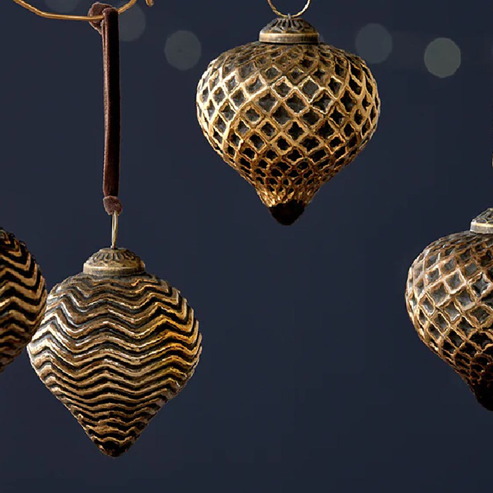Close up of black and gold glass teardrop baubles hanging from copper wire with cark velvet ribbon against a dark blue background
