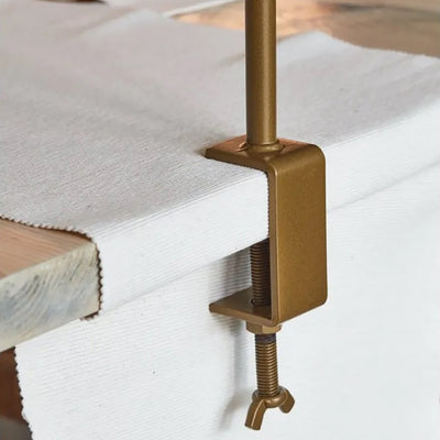 Fixing bolt of a over table display frame in gold that is screwed securely to the edge of a table with a white tablecloth underneath