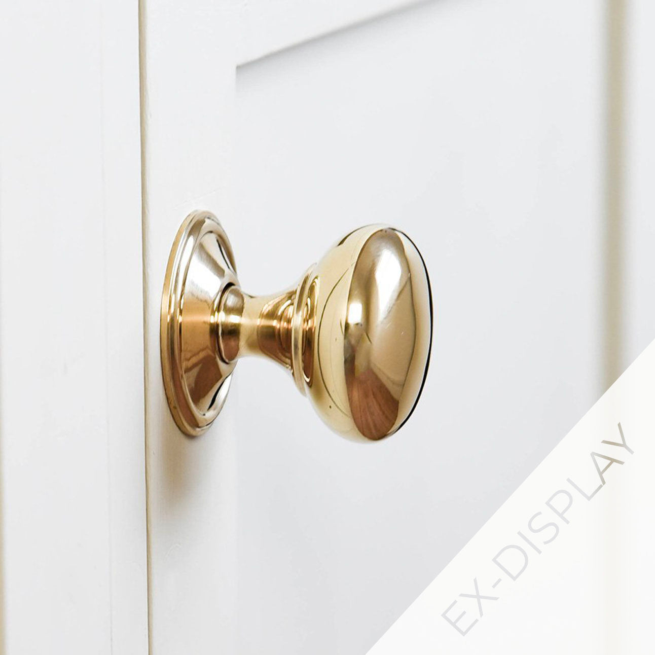 Polished brass cottage bun cabinet knob on a off-white background with an ex-display watermark in the corner