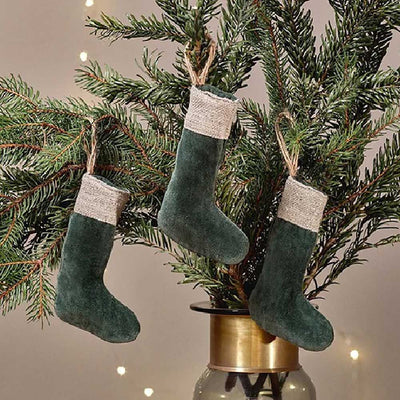 Forest green set of 3 mini stocking decorations made from velvet with a jute linen band at the top. Hanging from jute rope on Christmas tree sprigs against a pale background