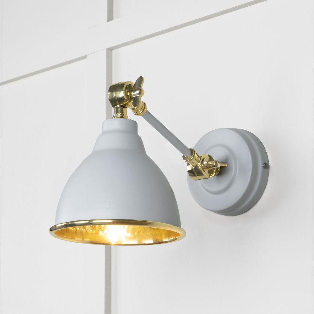 Hammered brass Brindley wall light in off-white against a white panelled wall