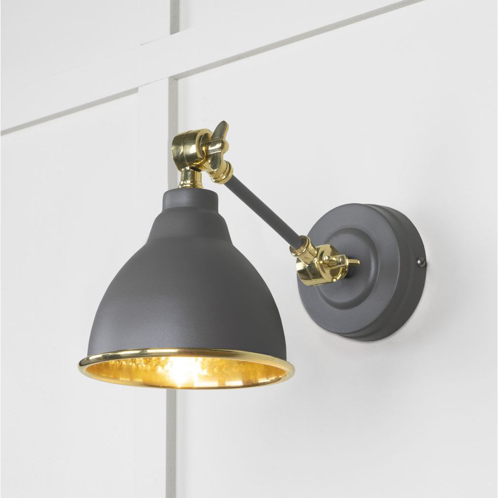 Hammered brass Brindley wall light in dark grey against a white panelled wall
