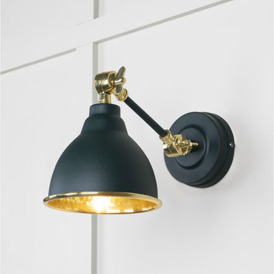 Hammered brass Brindley wall light in dark green against a white panelled wall