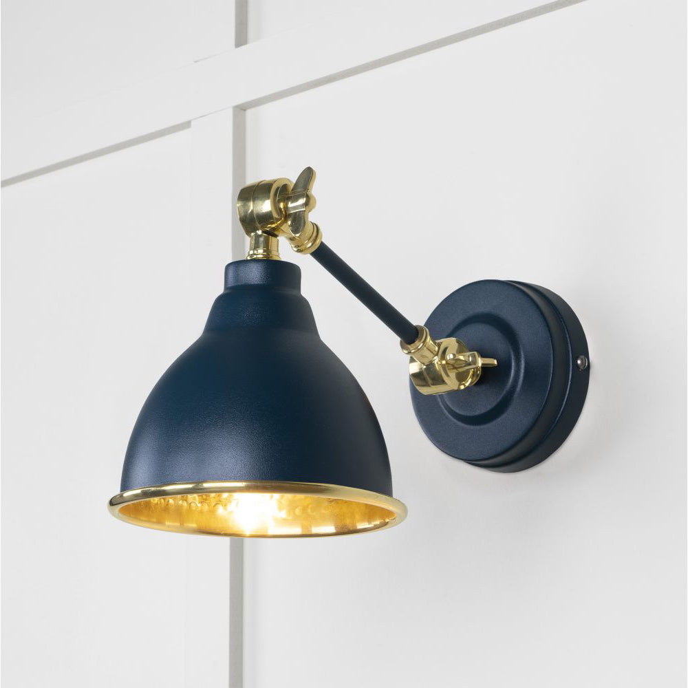 Hammered brass Brindley wall light in dark blue against a white panelled wall