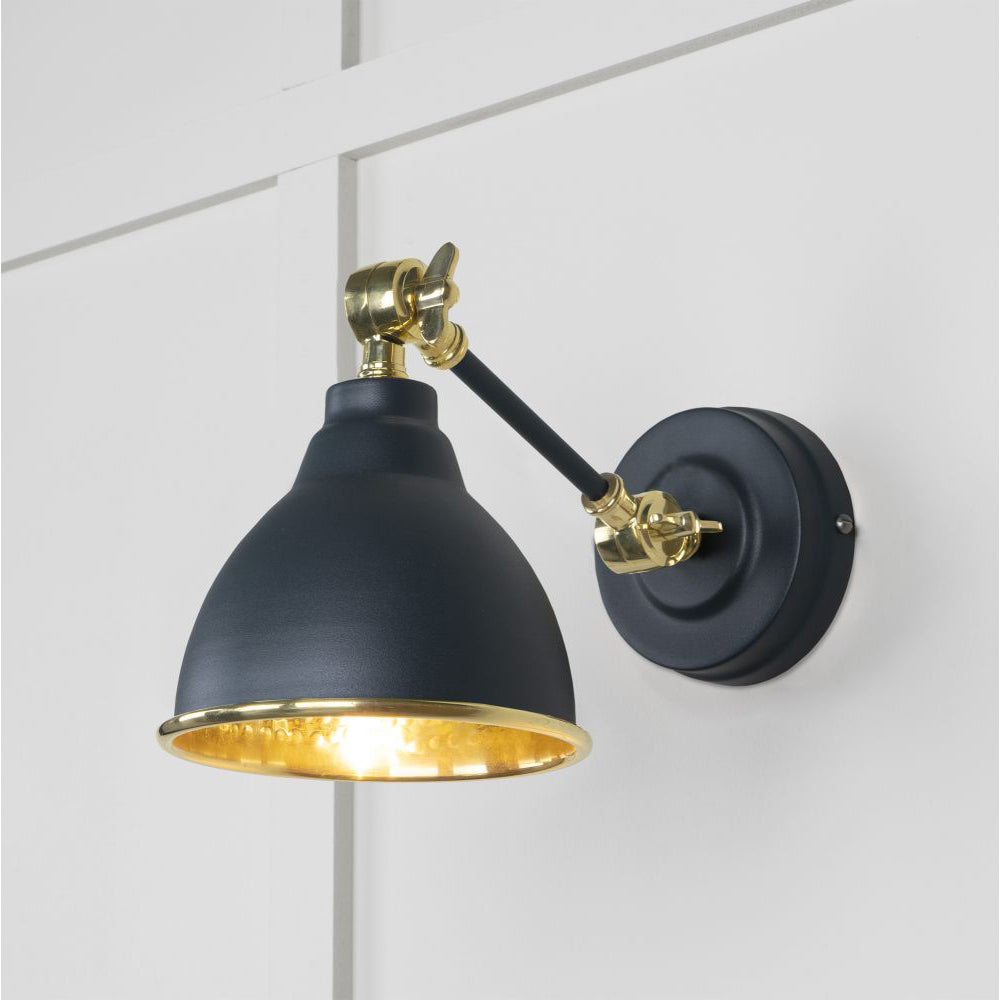Hammered brass Brindley wall light in blue-black against a white panelled wall