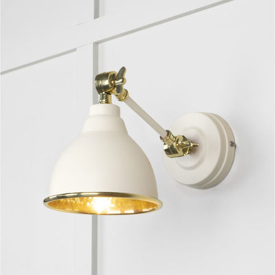 Hammered brass Brindley wall light in cream against a white panelled wall