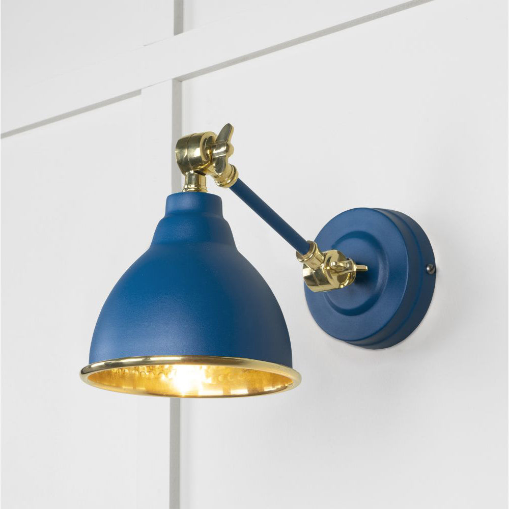 Hammered brass Brindley wall light in blue against a white panelled wall