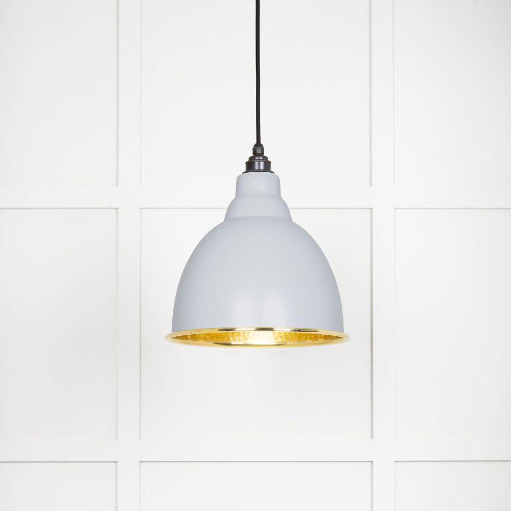 Hammered polished brass Brindley pendant light in birch hanging from a black fabric cord against a white panelled wall
