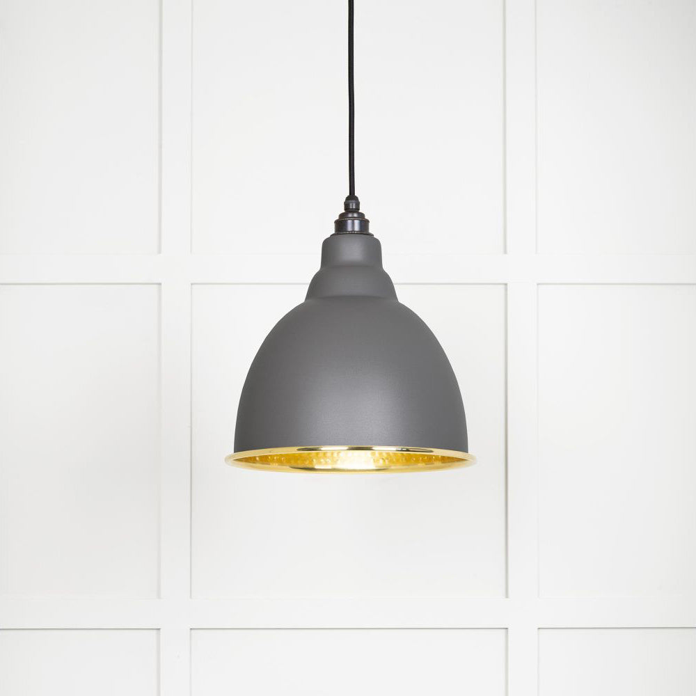 Hammered polished brass Brindley pendant light in bluff hanging from a black fabric cord against a white panelled wall