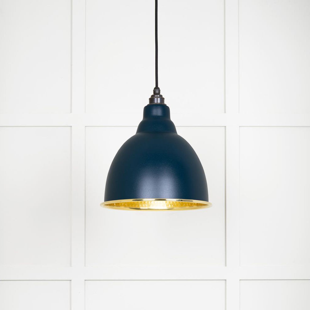Hammered polished brass Brindley pendant light in dusk hanging from a black fabric cord against a white panelled wall