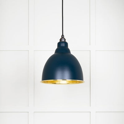 Hammered polished brass Brindley pendant light in dusk hanging from a black fabric cord against a white panelled wall