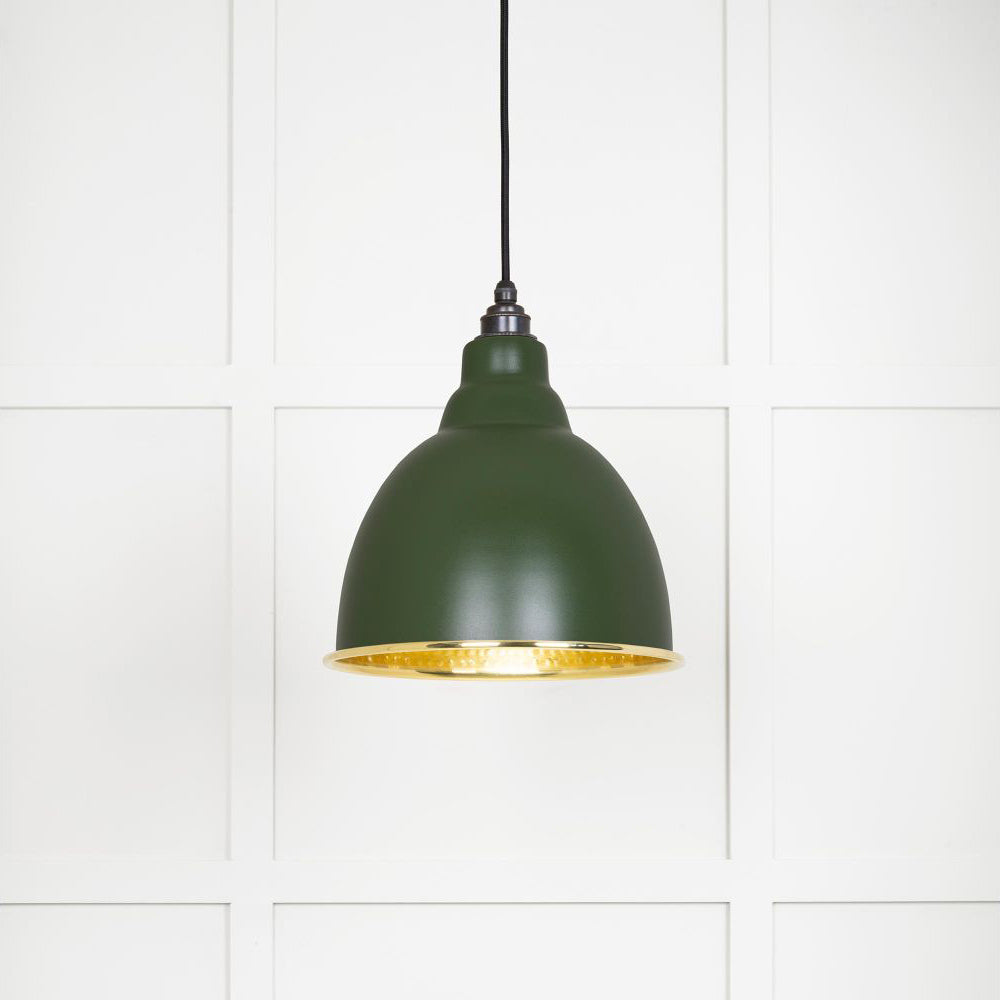 Hammered polished brass Brindley pendant light in heath hanging from a black fabric cord against a white panelled wall