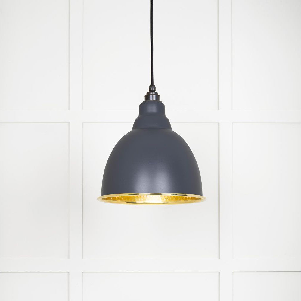 Hammered polished brass Brindley pendant light in slate hanging from a black fabric cord against a white panelled wall