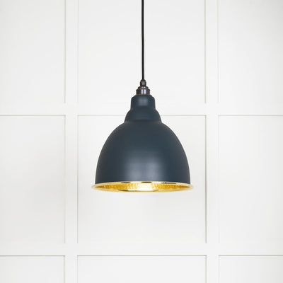 Hammered polished brass Brindley pendant light in soot hanging from a black fabric cord against a white panelled wall