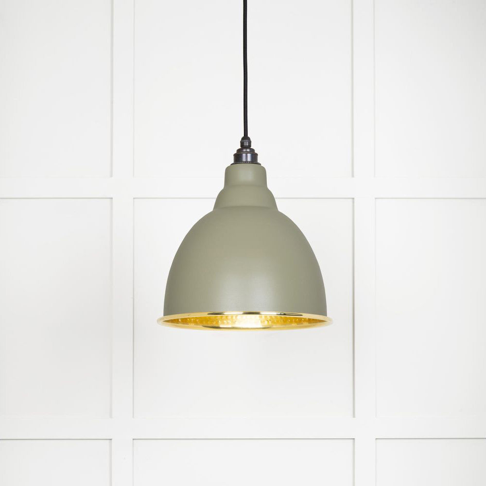 Hammered polished brass Brindley pendant light in tump hanging from a black fabric cord against a white panelled wall