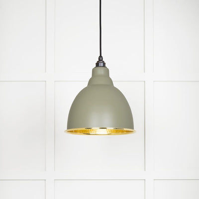 Hammered polished brass Brindley pendant light in tump hanging from a black fabric cord against a white panelled wall