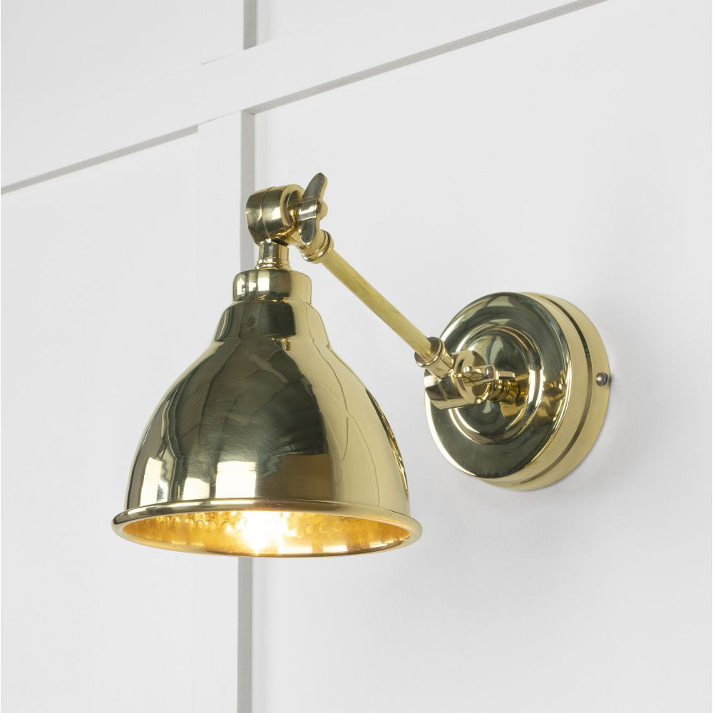 Polished brass wall light with internal hammered shade on white panelled wall