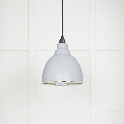 Hammered polished nickel Brindley pendant light in birch hanging from a black fabric cable against a white panelled wall
