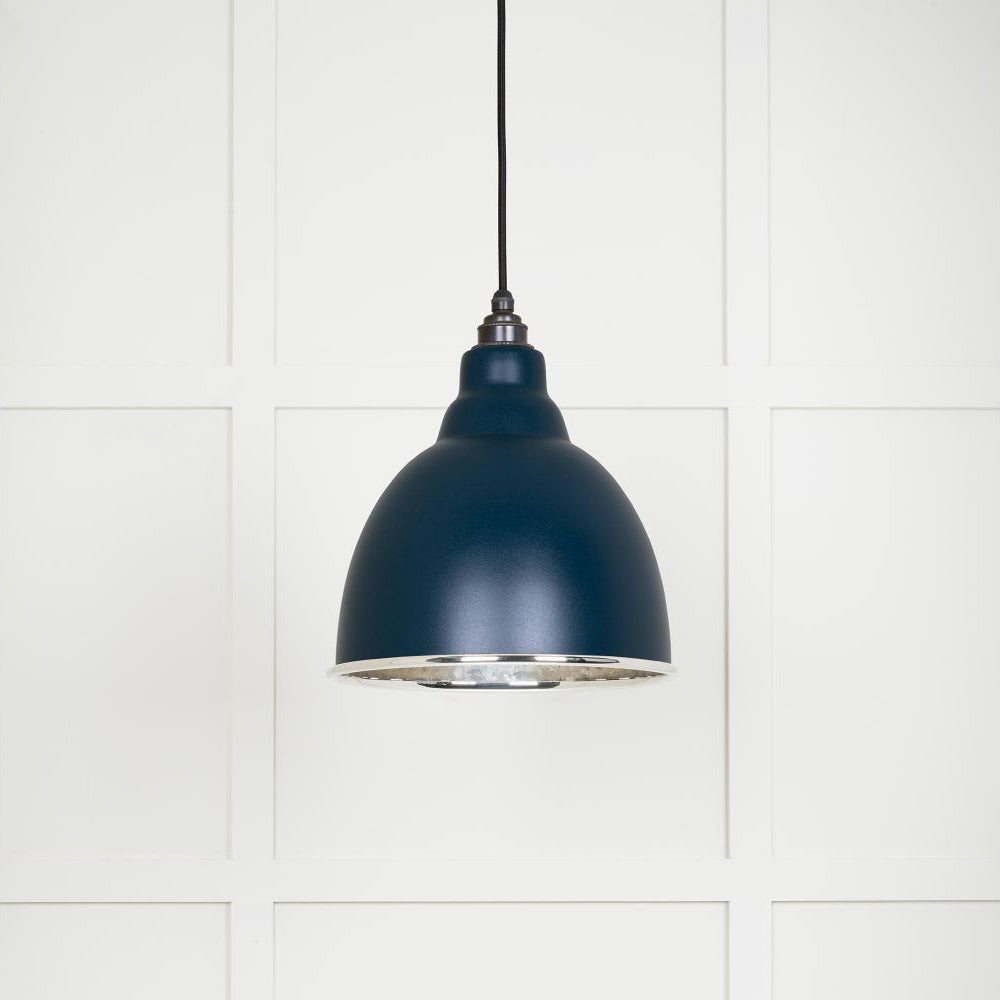 Hammered polished nickel Brindley pendant light in dusk hanging from a black fabric cable against a white panelled wall